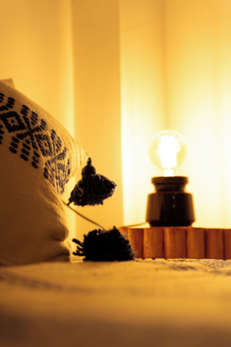 A bed with a patterned pillow and a small table with a light bulb.