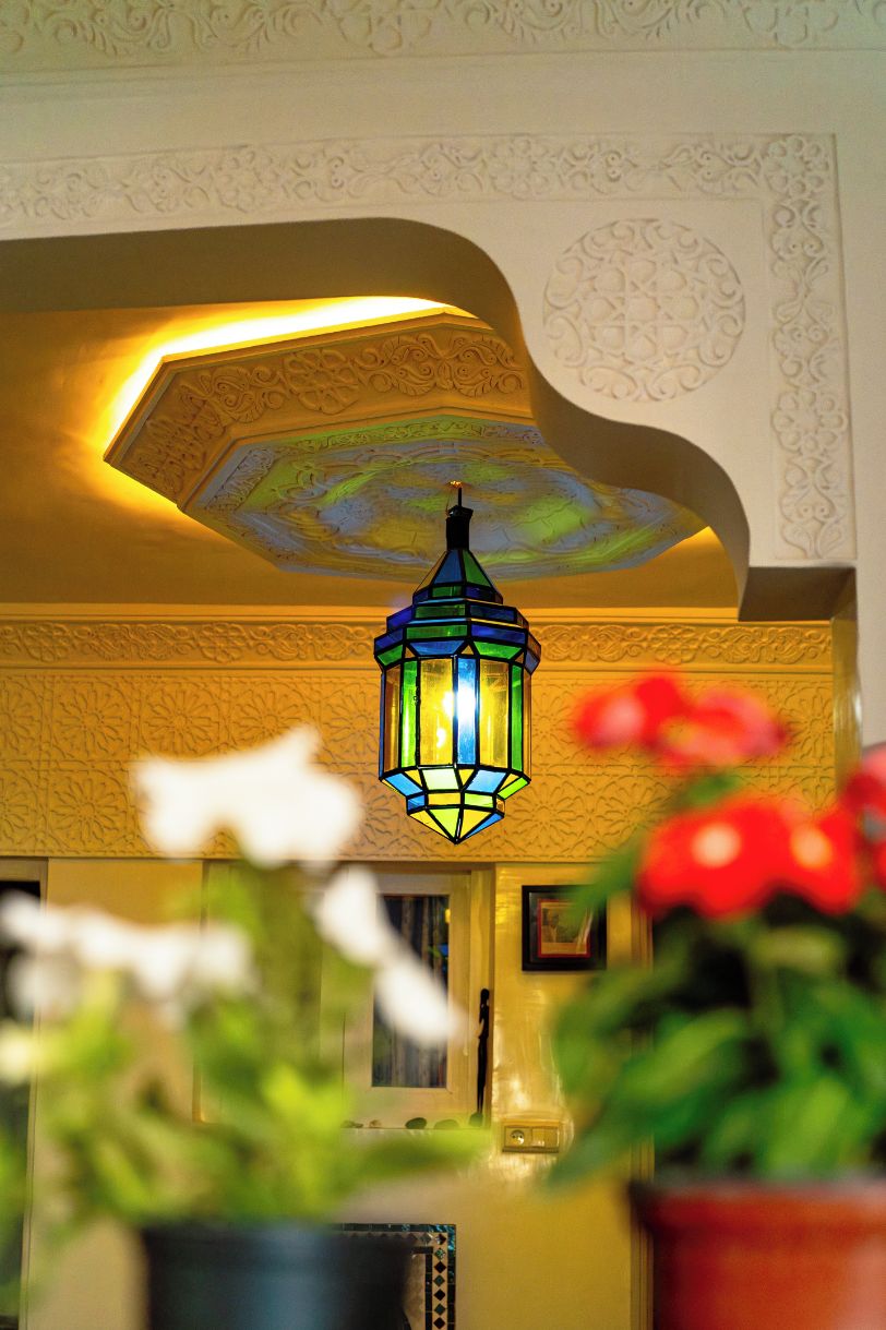 Eine farbige Glaslaterne hängt von einer verzierten Decke mit floralen Mustern.