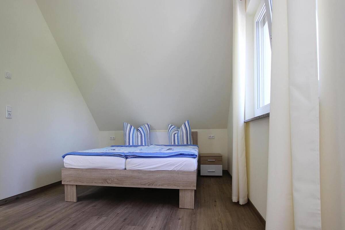A bedroom with a wooden bed, a nightstand, a drawer, and a window with curtains.