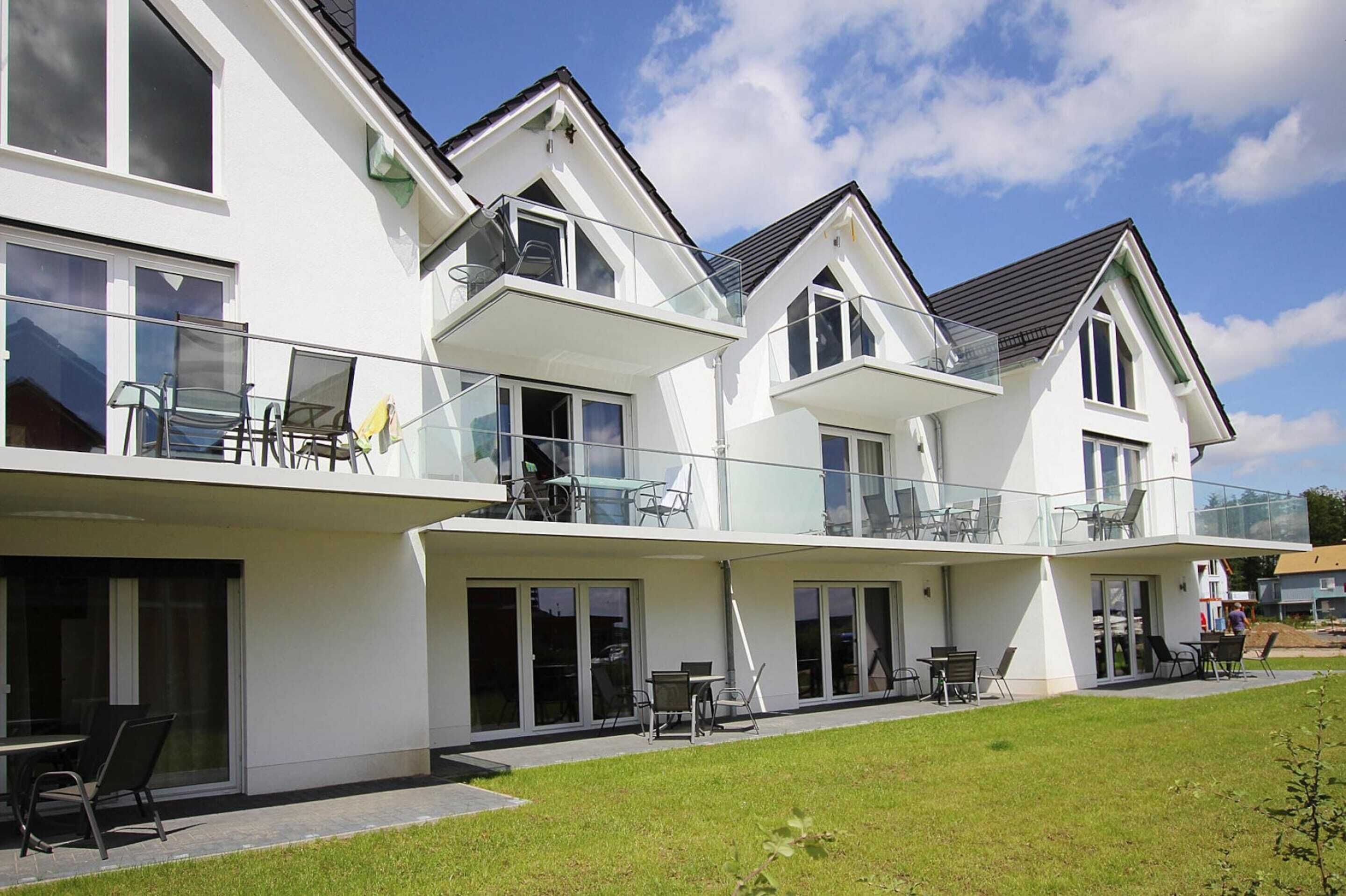 A modern two-story house with large glass windows, a balcony, and a well-maintained lawn.