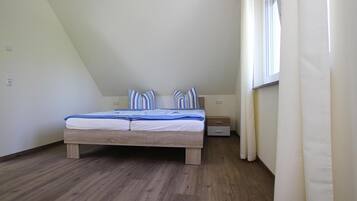 A bedroom with a wooden bed, a nightstand, a window with curtains, and a sloped ceiling.