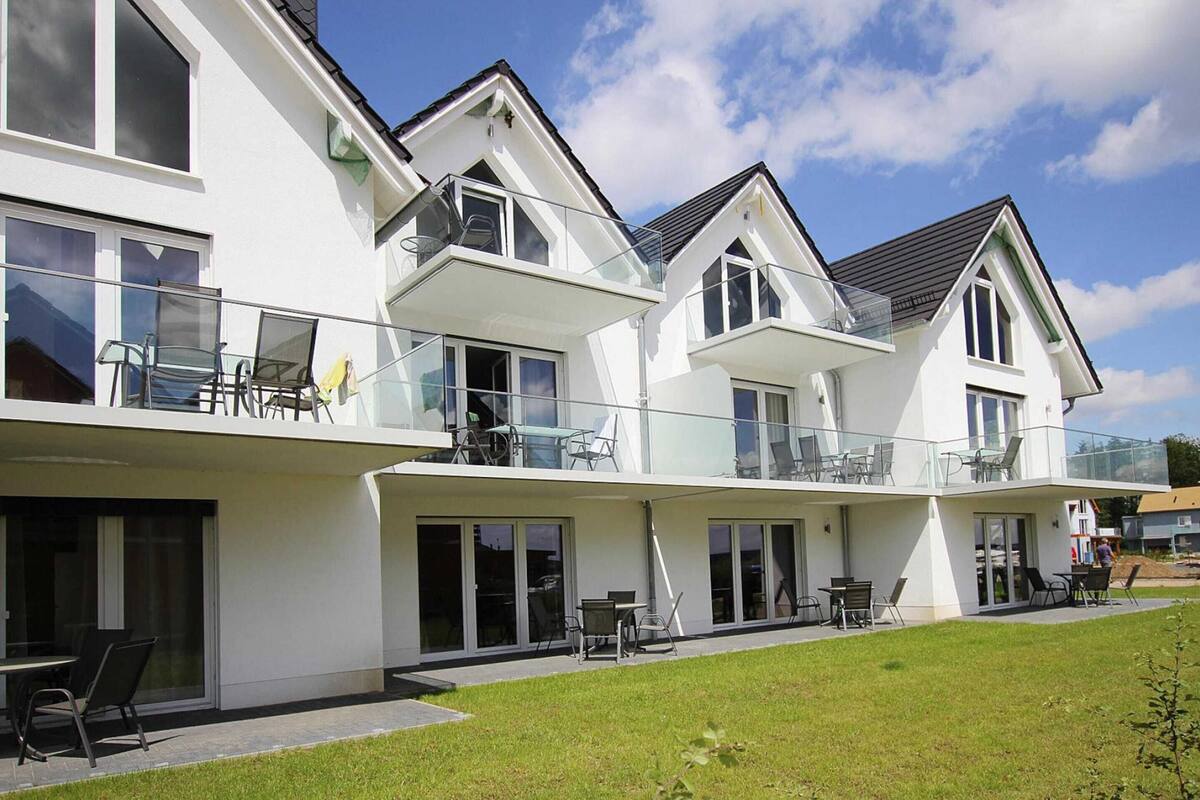 A modern two-story house with large glass windows, a balcony, and a well-maintained lawn.