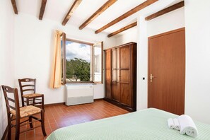 Ein Schlafzimmer mit Bett, Stuhl, Kleiderschrank, Fenster mit Vorhängen und Heizkörper.