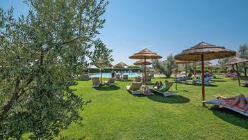 A poolside area with lounge chairs and umbrellas, a swimming pool, and a well-maintained lawn.