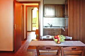 A dining area with a table set for two, a fruit bowl on the table, and a kitchen in the background.