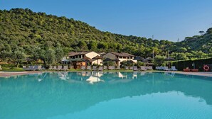 A swimming pool with lounge chairs and umbrellas, surrounded by buildings with a hilly backdrop. - Residence Le Corti di Montepitti, Suvereto (Suvereto)