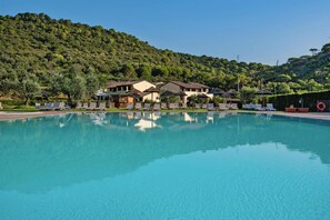 A swimming pool with lounge chairs and umbrellas, surrounded by buildings with a hilly backdrop. - Residence Le Corti di Montepitti, Suvereto (Suvereto)