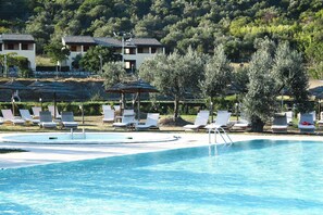 A pool with white lounge chairs and umbrellas, surrounded by trees and buildings.
