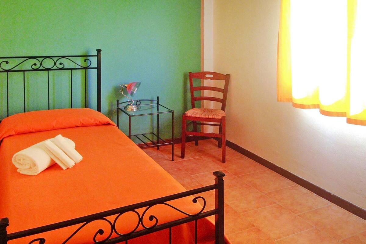 A room with a bed, a chair, a small table, and a window with curtains.