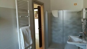 Un baño con ducha, lavamanos y una toalla colgada en un perchero.