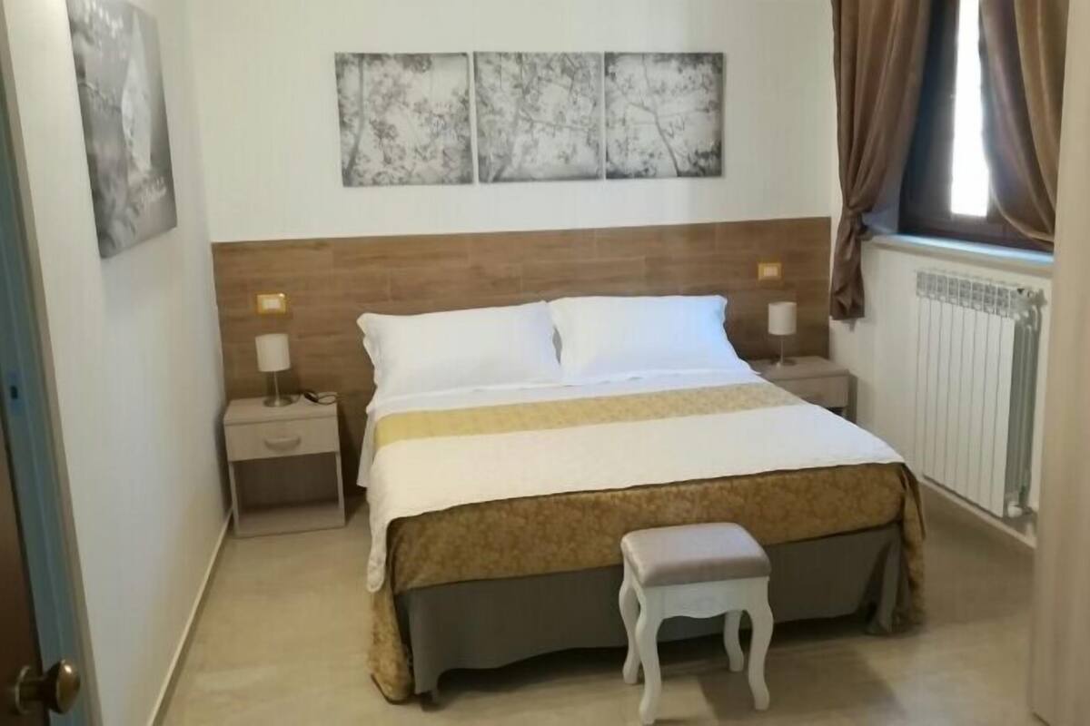 A bedroom with a bed, bedside tables, a bench, and artwork on the wall.