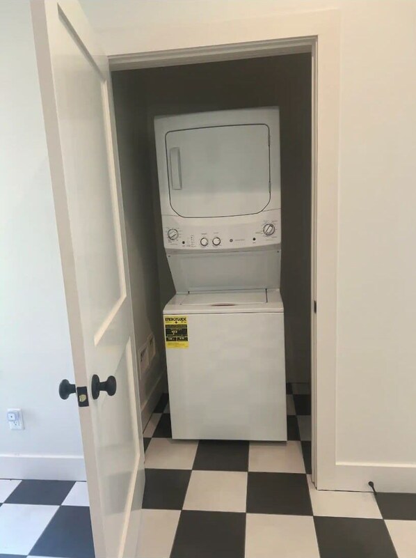 A compact washer and dryer unit in a narrow doorway with a checkered floor.