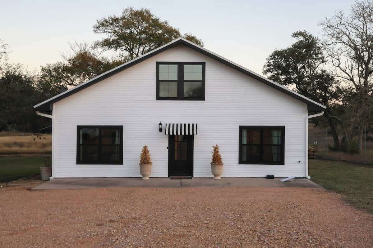 Et hvidt etplanshus med saddeltag, hoveddør og to store vinduer på hver side.