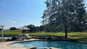 Une piscine avec un jacuzzi, entourée d’une terrasse en pierre et de chaises longues.