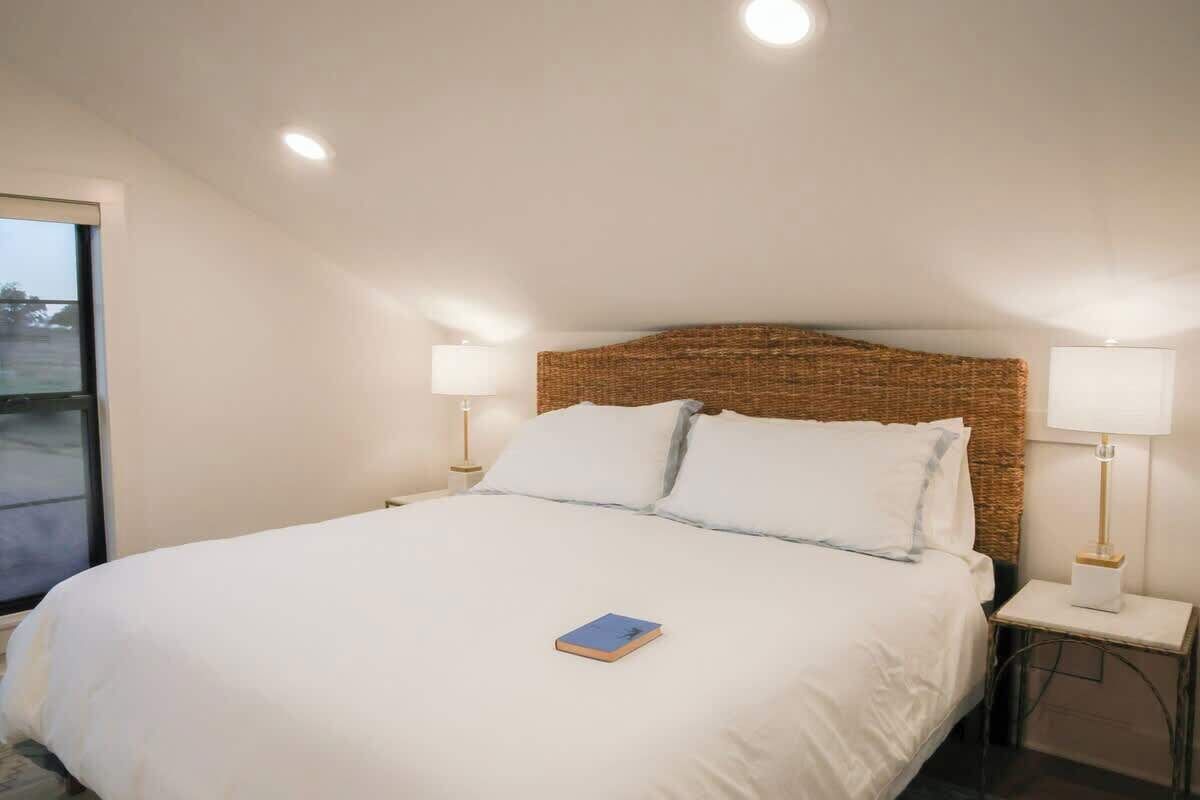 A neatly made bed with white linens, a blue book on the bed, and two bedside lamps on matching nightstands.