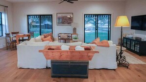 Un salon spacieux avec un grand canapé, une table basse et un téléviseur. De grandes fenêtres offrent une vue sur l’extérieur.