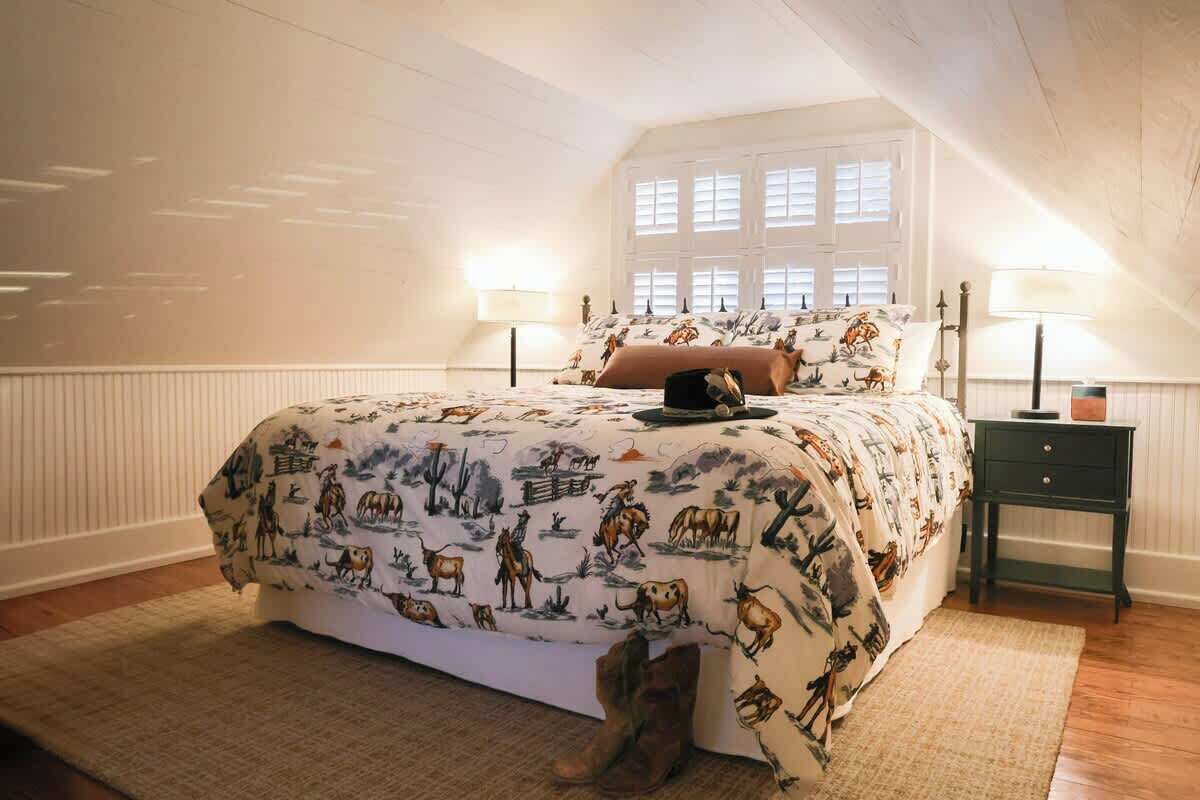Un dormitorio con una cama grande, dos lámparas de noche, una mesita de noche y una ventana con contraventanas.