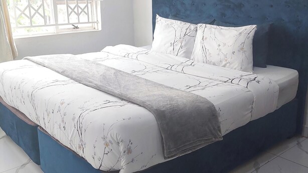 A bedroom with a large bed, a blue headboard, and a window with a view of greenery.