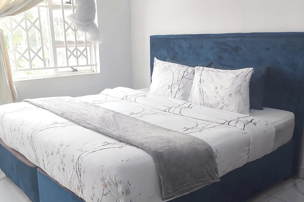 Une chambre avec un grand lit, une tête de lit bleue et une fenêtre donnant sur un paysage verdoyant.