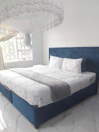 A bedroom with a large bed, a blue headboard, and a window with a view of greenery.