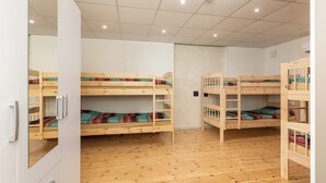 Una habitación con tres literas, suelo de madera y una puerta blanca con espejo.