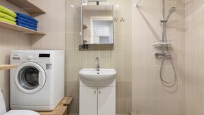 Un baño pequeño equipado con lavadora, lavamanos y ducha.