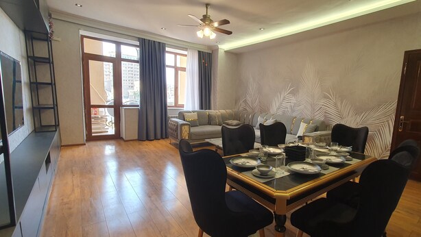 A dining area with a wooden table set for four, a sofa, and a decorative wall. - The Pearl of Nizami Street (Baku)