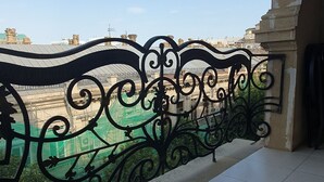 A balcony with a decorative metal railing, a tiled floor, and a view of buildings in the distance. - The Pearl of Nizami Street (Baku)