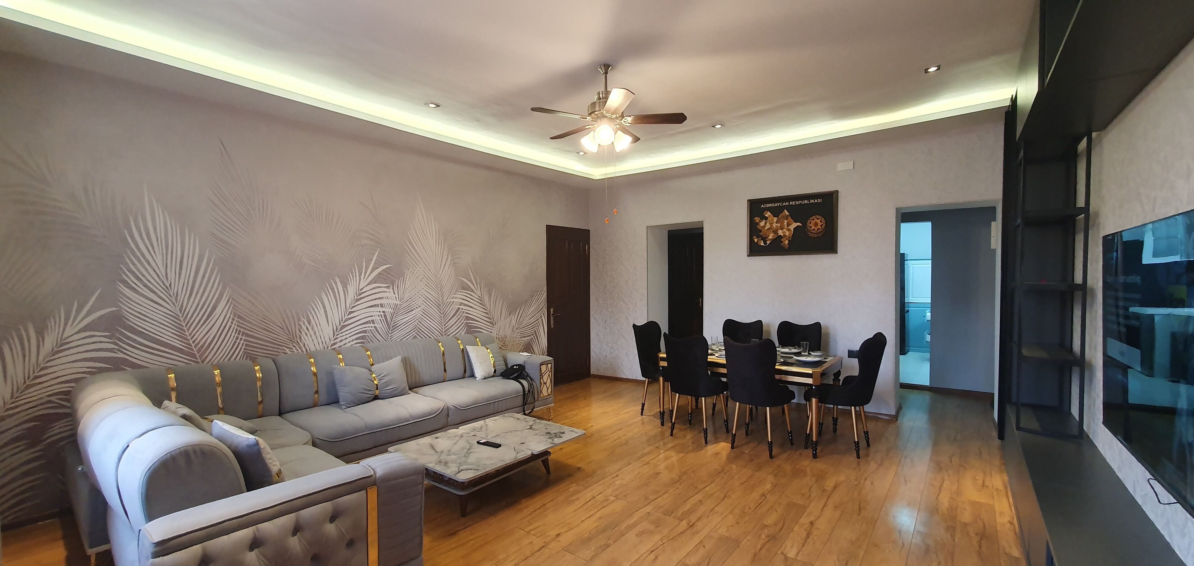 Una sala de estar moderna con un sofá gris, una mesa de comedor con sillas y un ventilador de techo.