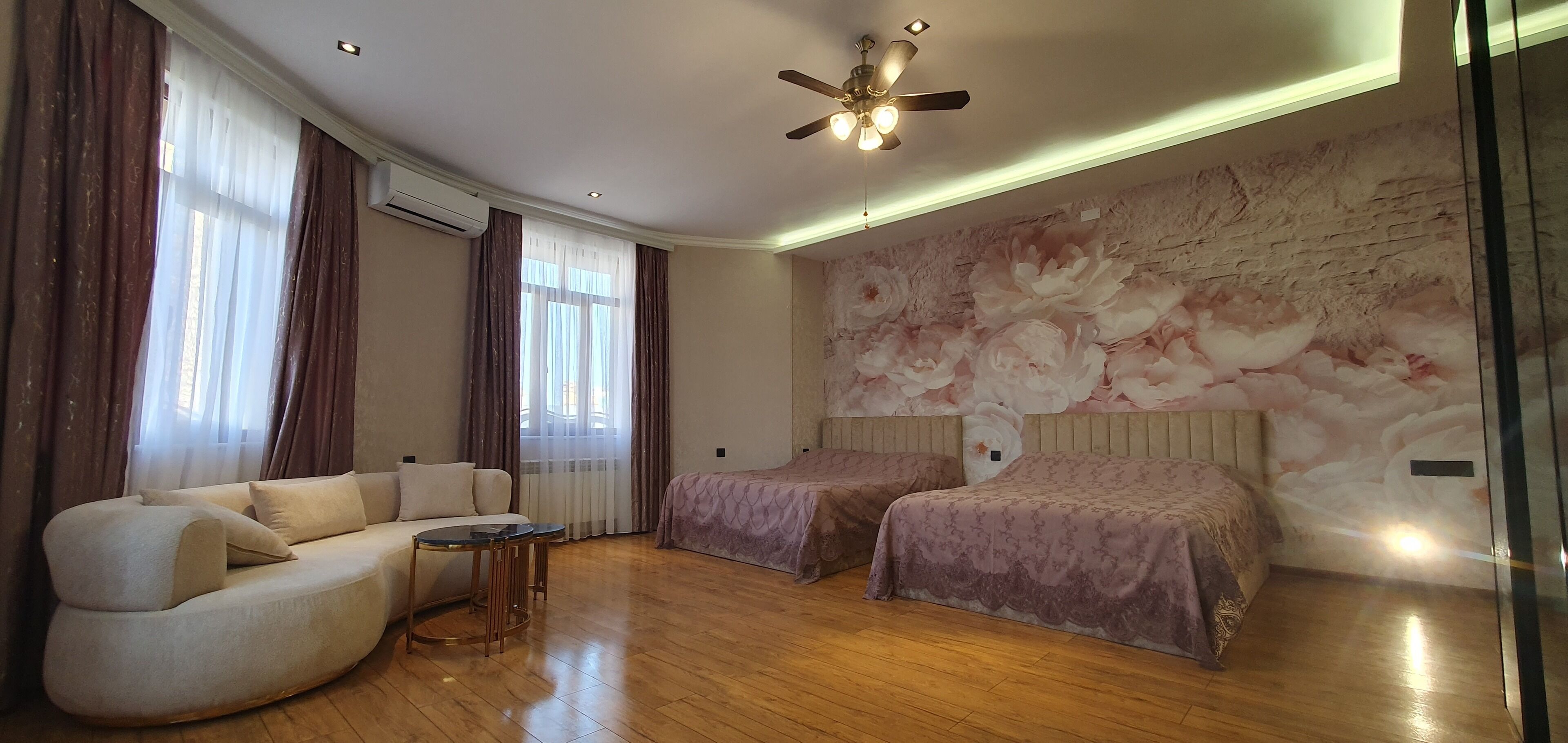 Une chambre moderne avec un canapé, deux lits, un ventilateur de plafond et un grand décor mural représentant des motifs floraux.