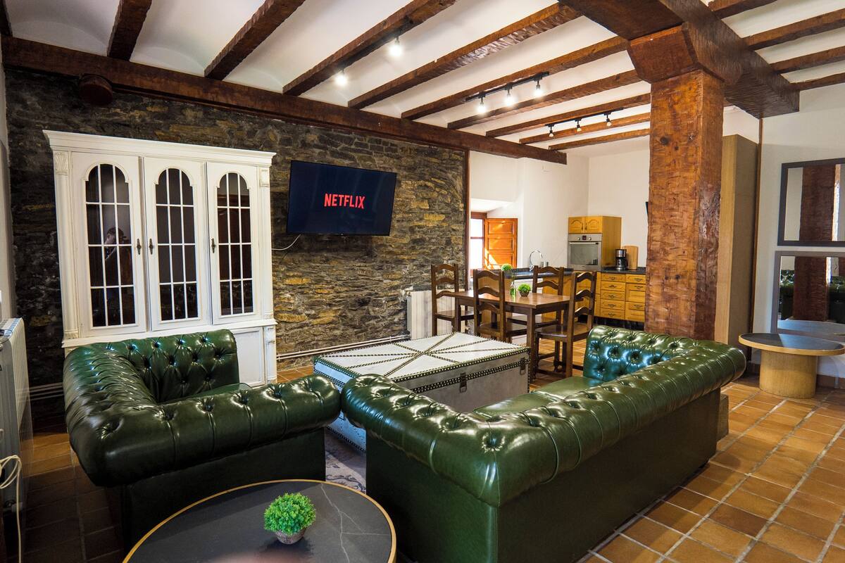Uma sala de estar aconchegante com um sofá de couro verde, uma parede de pedra e uma TV Netflix montada na parede.
