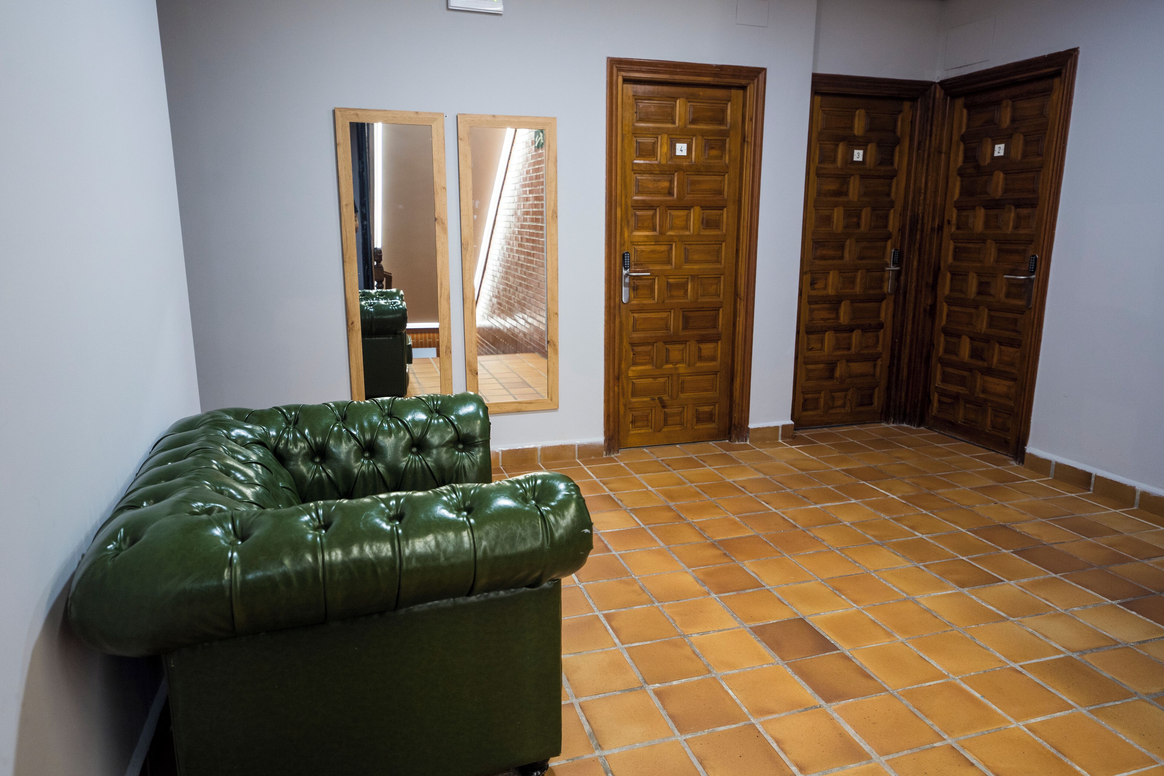 Una habitación con un sofá de cuero verde, dos puertas de madera y suelo de baldosas.