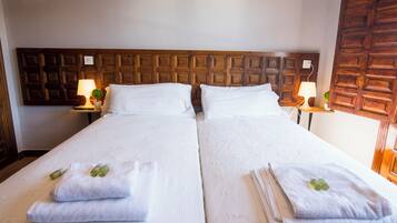 Una cama doble con sábanas blancas y dos almohadas, un cabecero de madera, dos mesitas de noche con lámparas y una puerta de madera.
