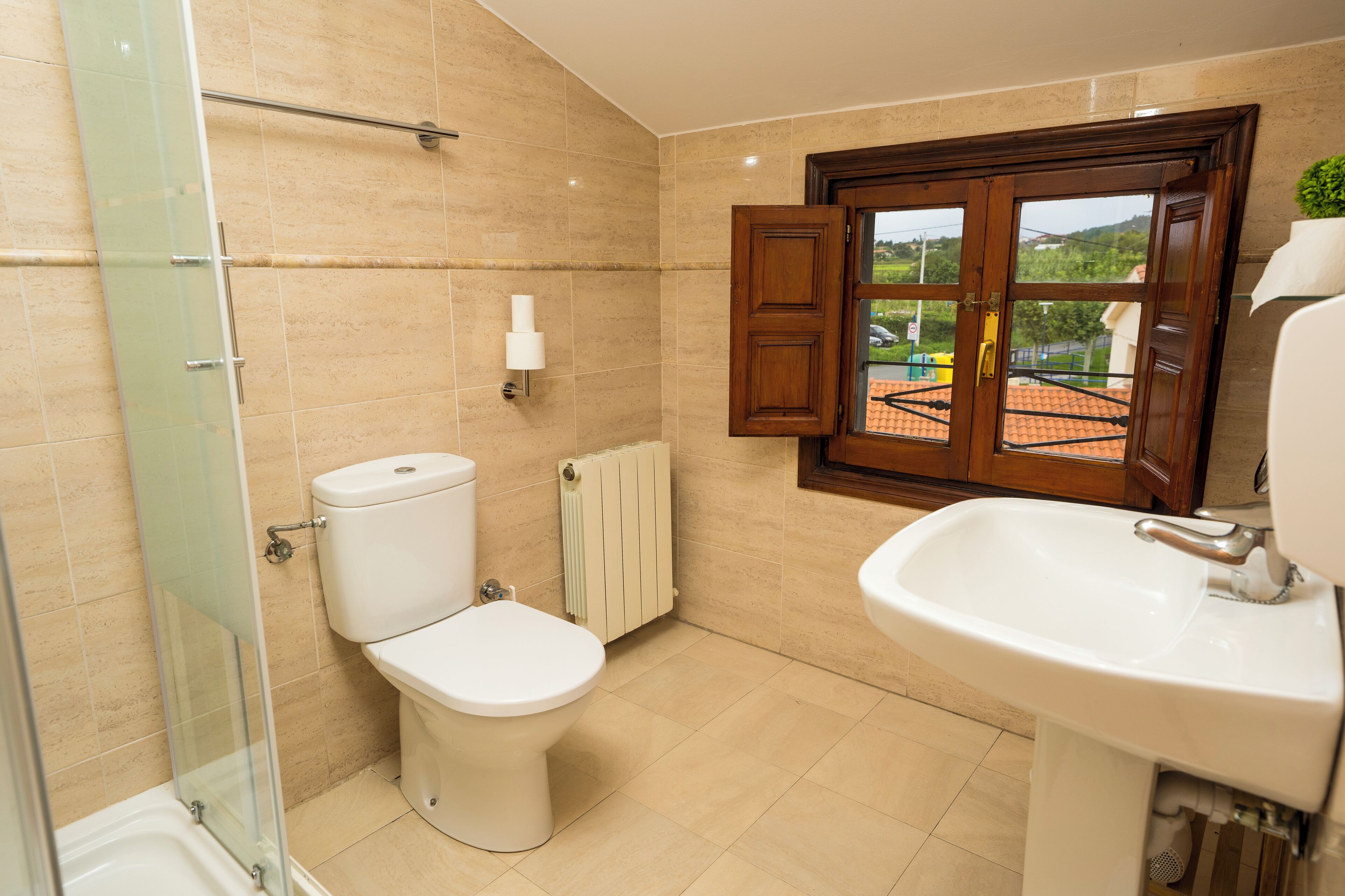 A bathroom with a toilet, a sink, a glass shower enclosure, and a window with an open door.