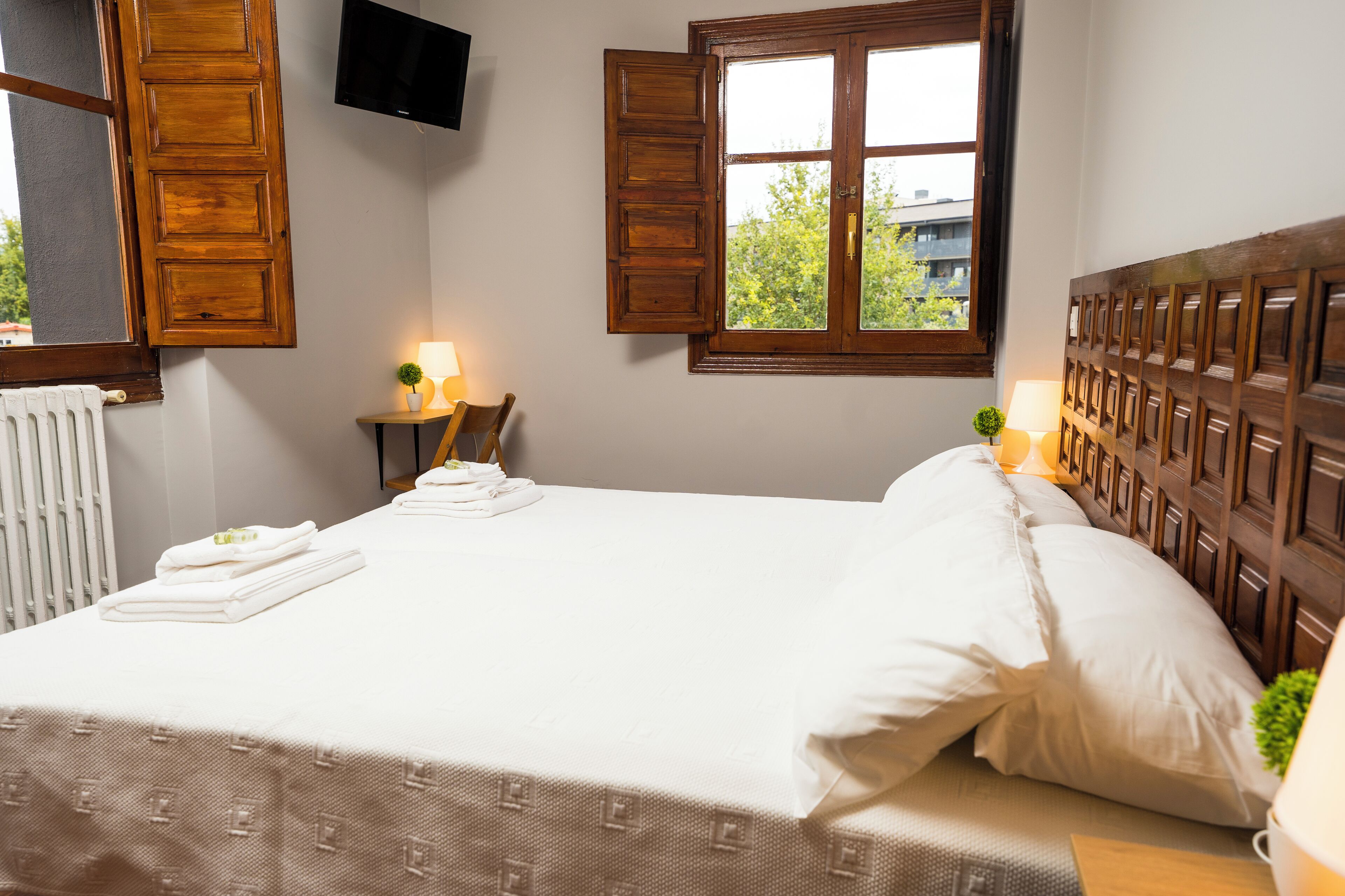 Ein ordentlich bezogenes Bett mit weißen Leinen, einem Holz-Kopfende und einem Fenster mit Rollläden.