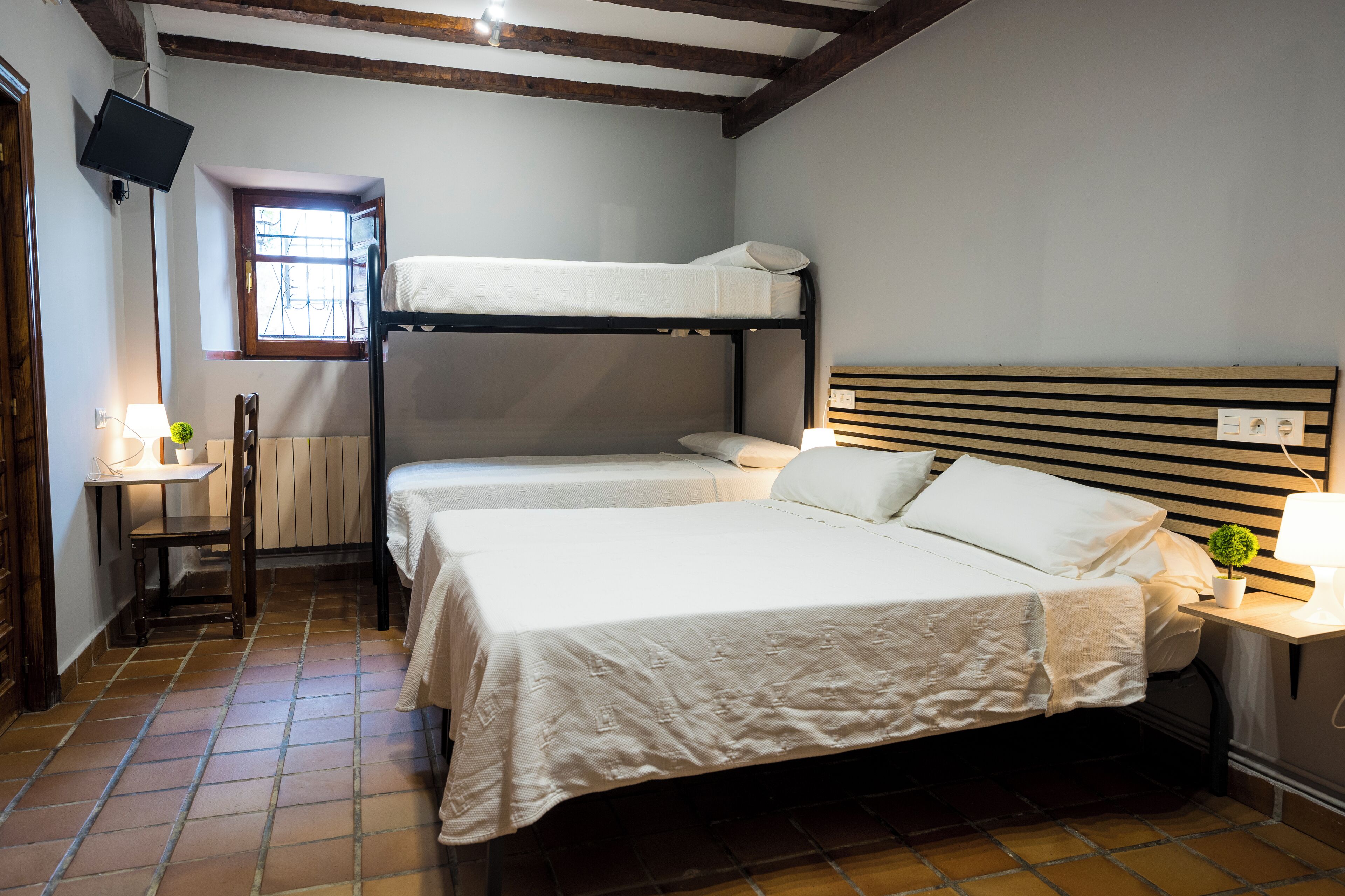 A room with a bunk bed, a desk with a lamp, a chair, and a small plant.