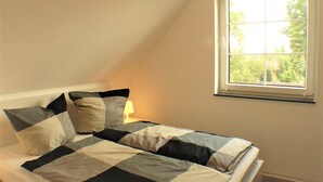Un dormitorio con colcha a cuadros, una ventana con vistas a zonas verdes y una lámpara de noche.