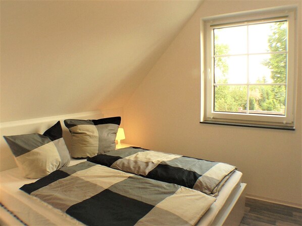 A bedroom with a checkered bedspread, a window with a view of greenery, and a bedside lamp.