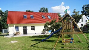 Una casa con techo rojo, un parque infantil de madera y un jardín pequeño.