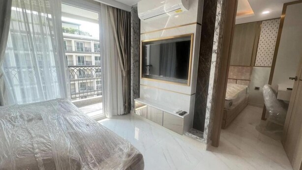 Una habitación de hotel moderna con una cama grande, un televisor montado en la pared y un balcón con cortinas.