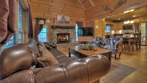 A cozy cabin interior with a stone fireplace, leather sofa, and a dining area. - Pet-friendly, family-sized, hot tub, firepit, pool table, WiFi (Blairsville)