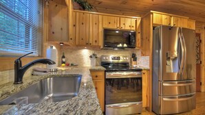 A modern kitchen with wooden cabinets, stainless steel appliances, granite countertops, and a window with blinds. - Pet-friendly, family-sized, hot tub, firepit, pool table, WiFi (Blairsville)