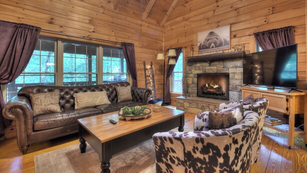 A cozy living room with a stone fireplace, leather sofas, and a television. - Pet-friendly, family-sized, hot tub, firepit, pool table, WiFi (Blairsville)