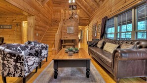 A log cabin interior with a staircase, two sofas, and a coffee table. - Pet-friendly, family-sized, hot tub, firepit, pool table, WiFi (Blairsville)