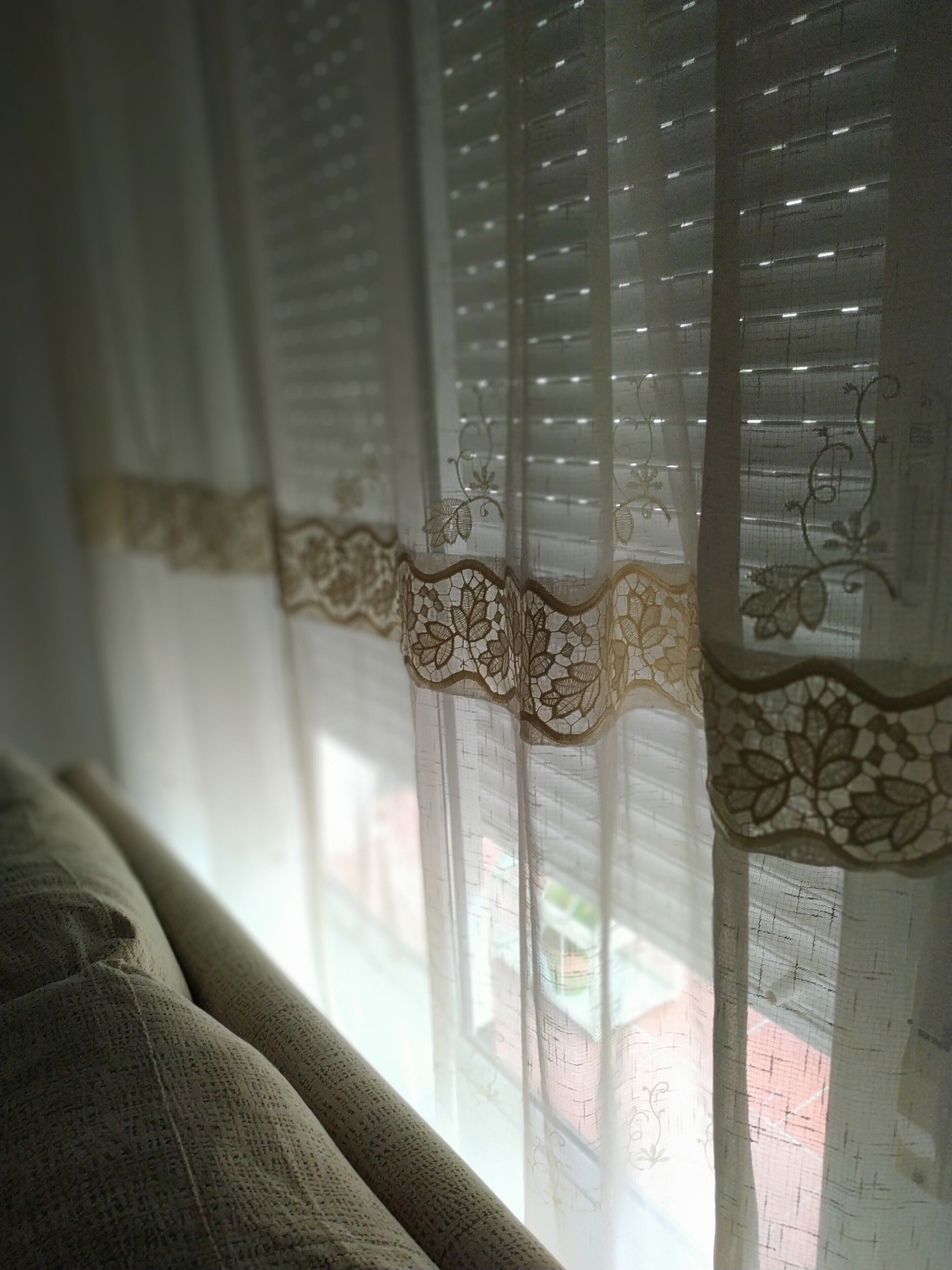 A window with sheer curtains featuring a floral pattern and a textured fabric visible on the window sill.