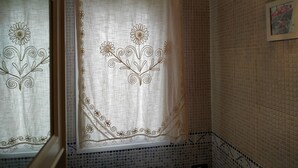 A bathroom with a white shower curtain featuring floral embroidery, tiled walls, and a hanging light fixture.