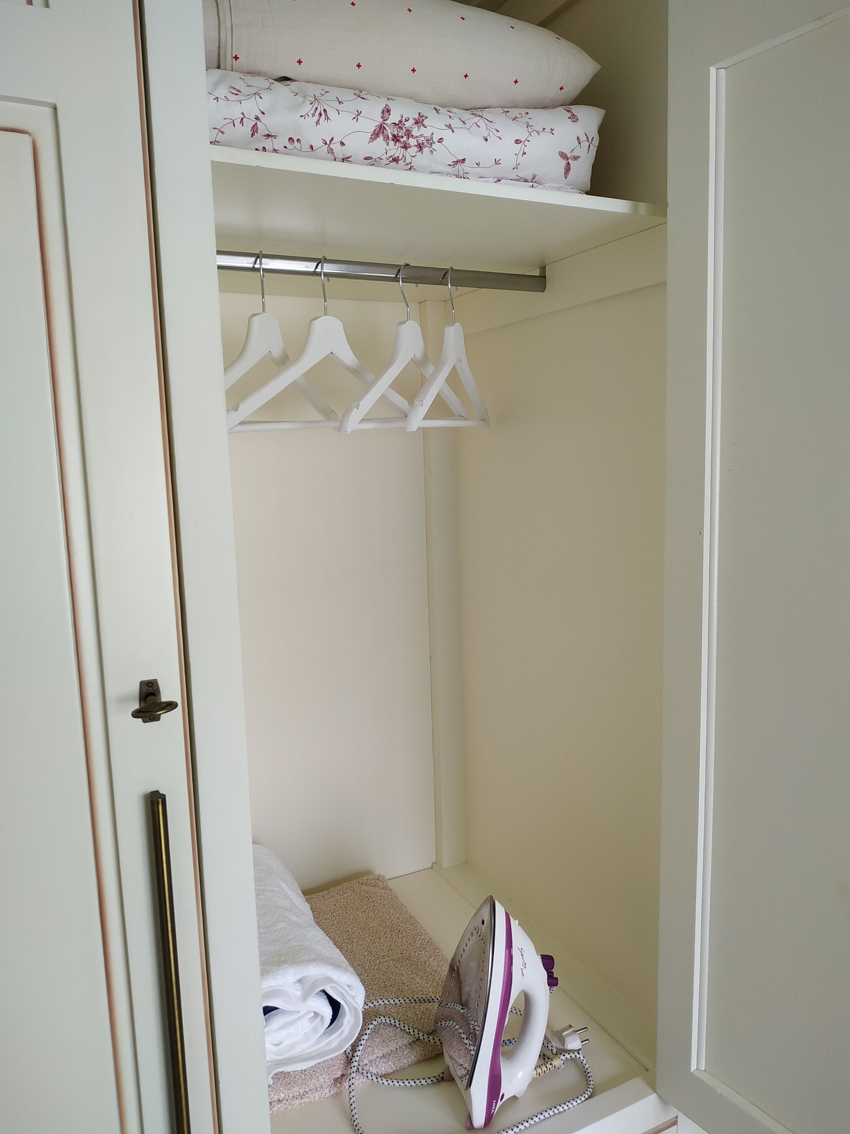 A bedroom with a bed, a hanging laundry rack, and an ironing board with an iron.