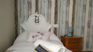 A neatly made bed with a rolled-up book, a wooden nightstand with a lamp, and a wall with vertical wooden planks.