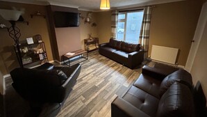 A living room with a sofa, a coffee table, and a TV mounted on the wall. - 2bedroom-1bathroom-patio-wifi (Auchterarder)