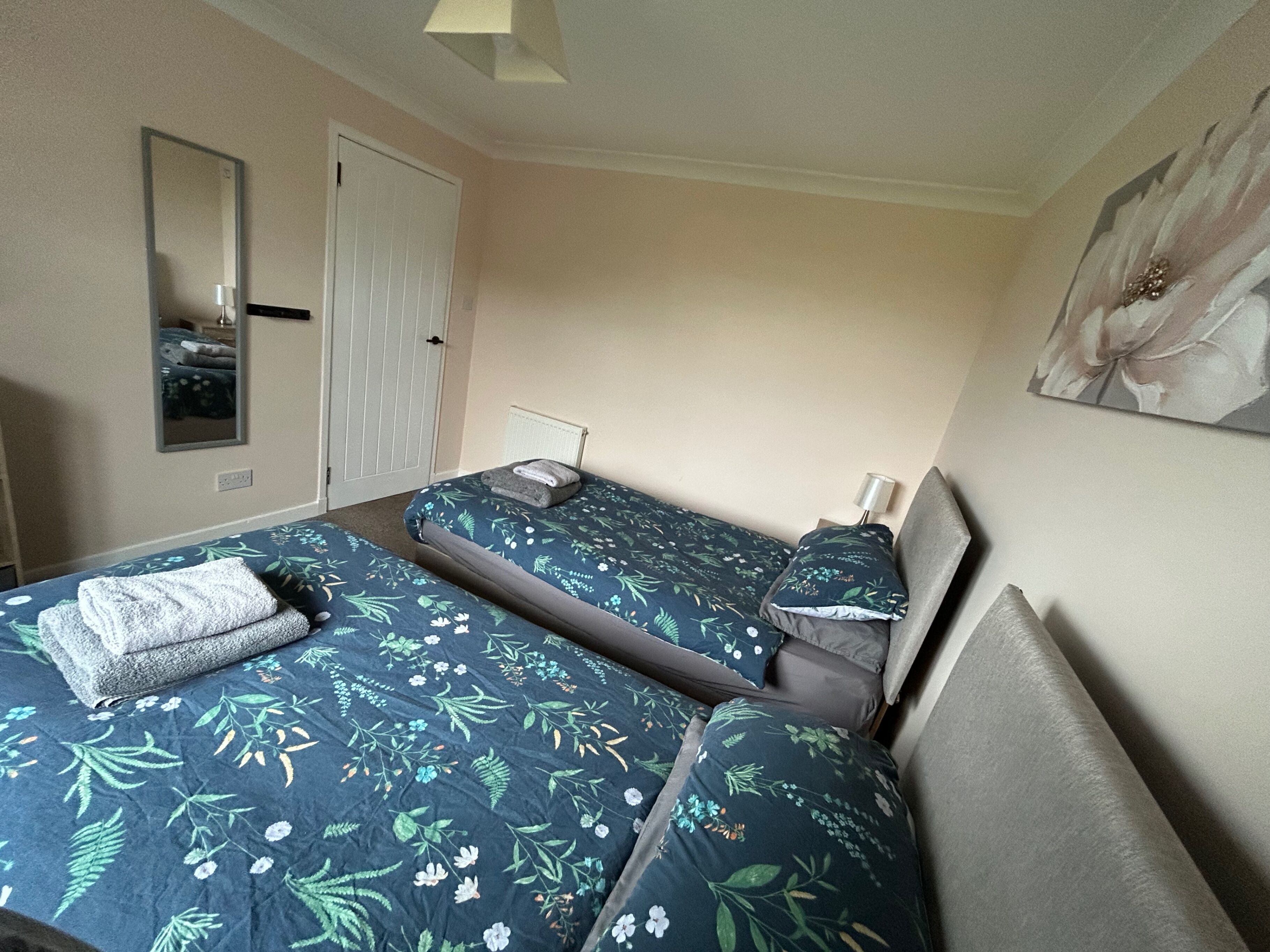 Een kamer met twee bedden, een spiegel, een deur en een schilderij aan de muur.
